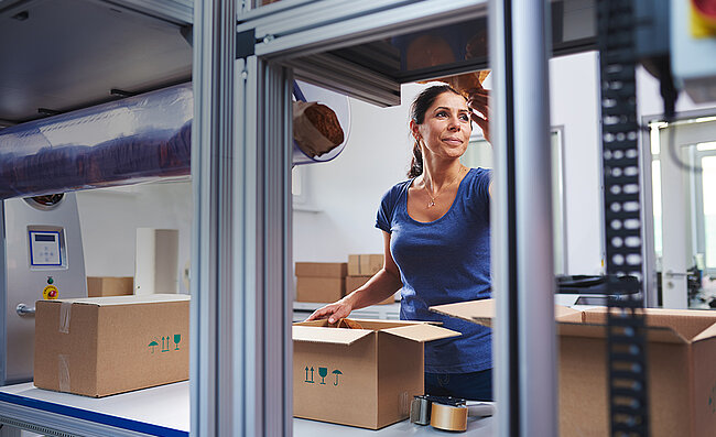 Een vrouw verpakt producten bij een verpakkingsstation in een kartonnen doos 